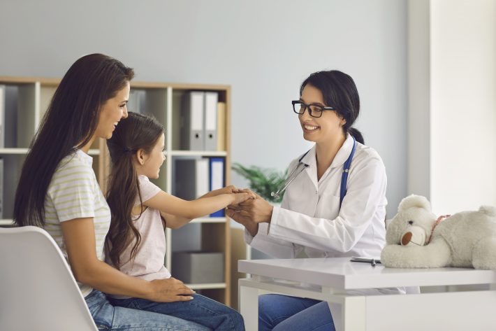 Mother and child at the doctor’s office for a preventive care appointment, covered by their health insurance plan as one of the essential health benefits.