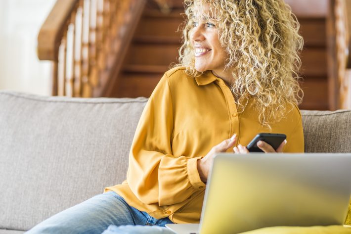 A blonde haired woman smiling and looking at her phone.