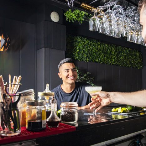 A Latin American Customer At A Bar Receives A Drink From The Wai