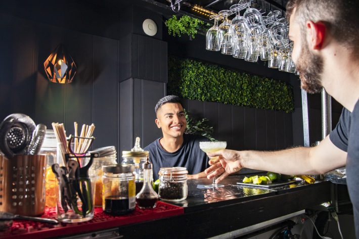 A Latin American Customer At A Bar Receives A Drink From The Wai