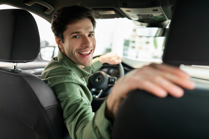 Cheerful Young Man Driving New Automobile After Purchase, Sittin