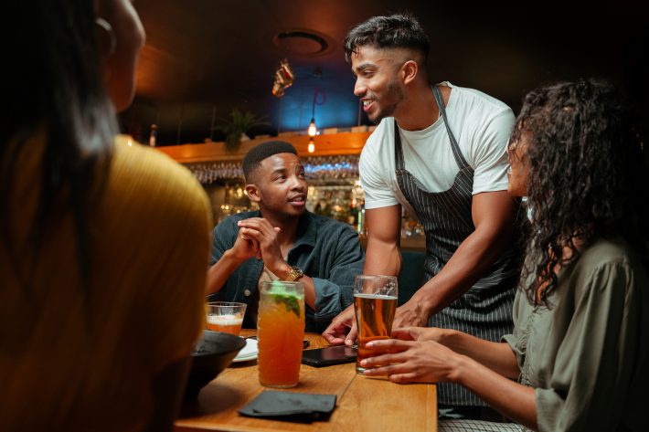 Diverse Group Of Friends Out For Dinner Being Served By Waiter