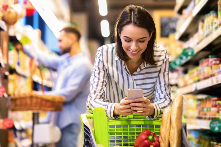 Smiling Female Customer Doing Grocery Shopping Using Smartphone