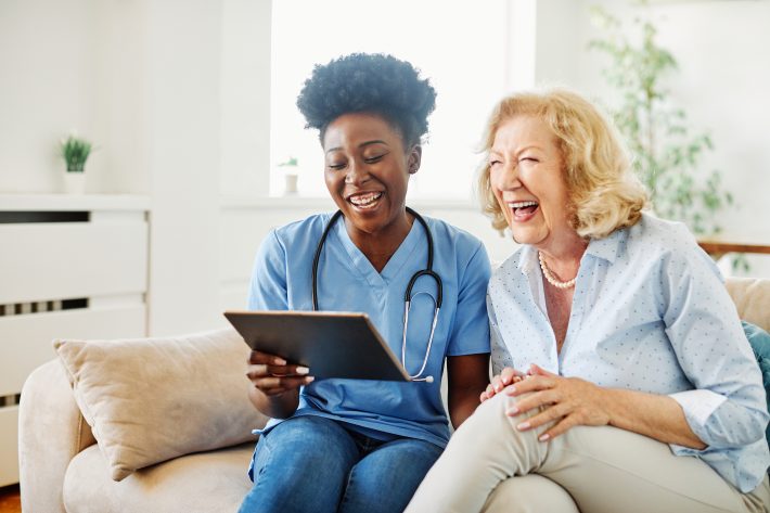 Doctor Or Nurse Caregiver Showing A Tablet Screen To Senior Woma