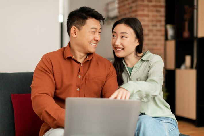 Positive Asian Man And Woman Using Laptop, Shopping Online Or Ha