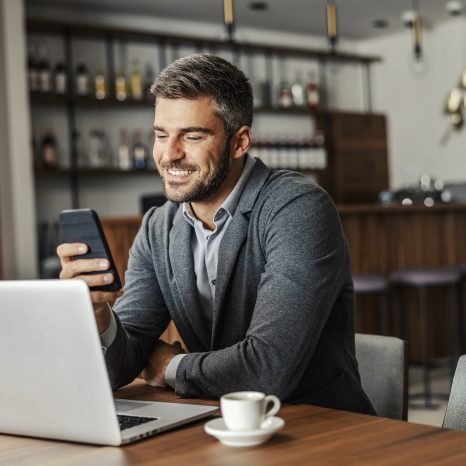 A Happy Businessman Is Sitting In A Coffee Shop And Checking On