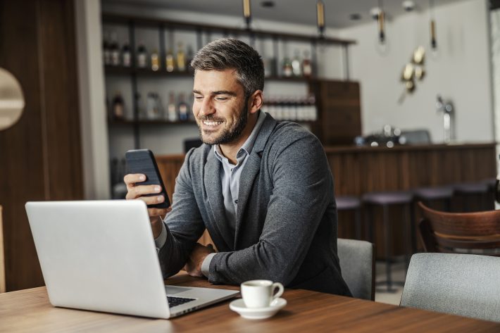 A Happy Businessman Is Sitting In A Coffee Shop And Checking On