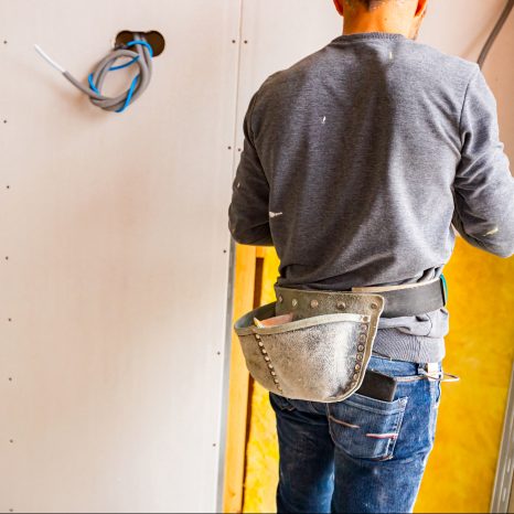 Shot From Behind Of Worker With Tool Bag Around His Waist, Works